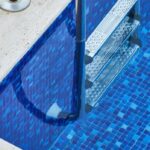 Detailaufnahme von Beckenrandsteinen und einer Edelstahl-Pooltreppe mit rutschfesten Stufen